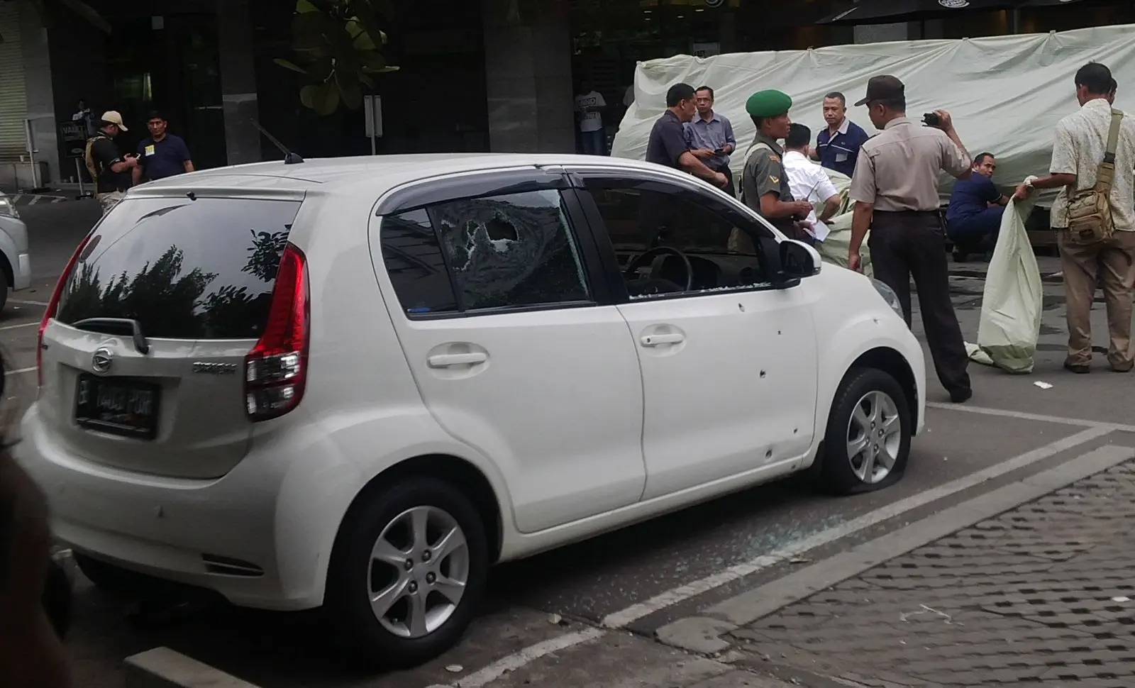 Kristin's white Daihatsu Sirion with its rear window shot through, tarpaulins screening the dead behind it